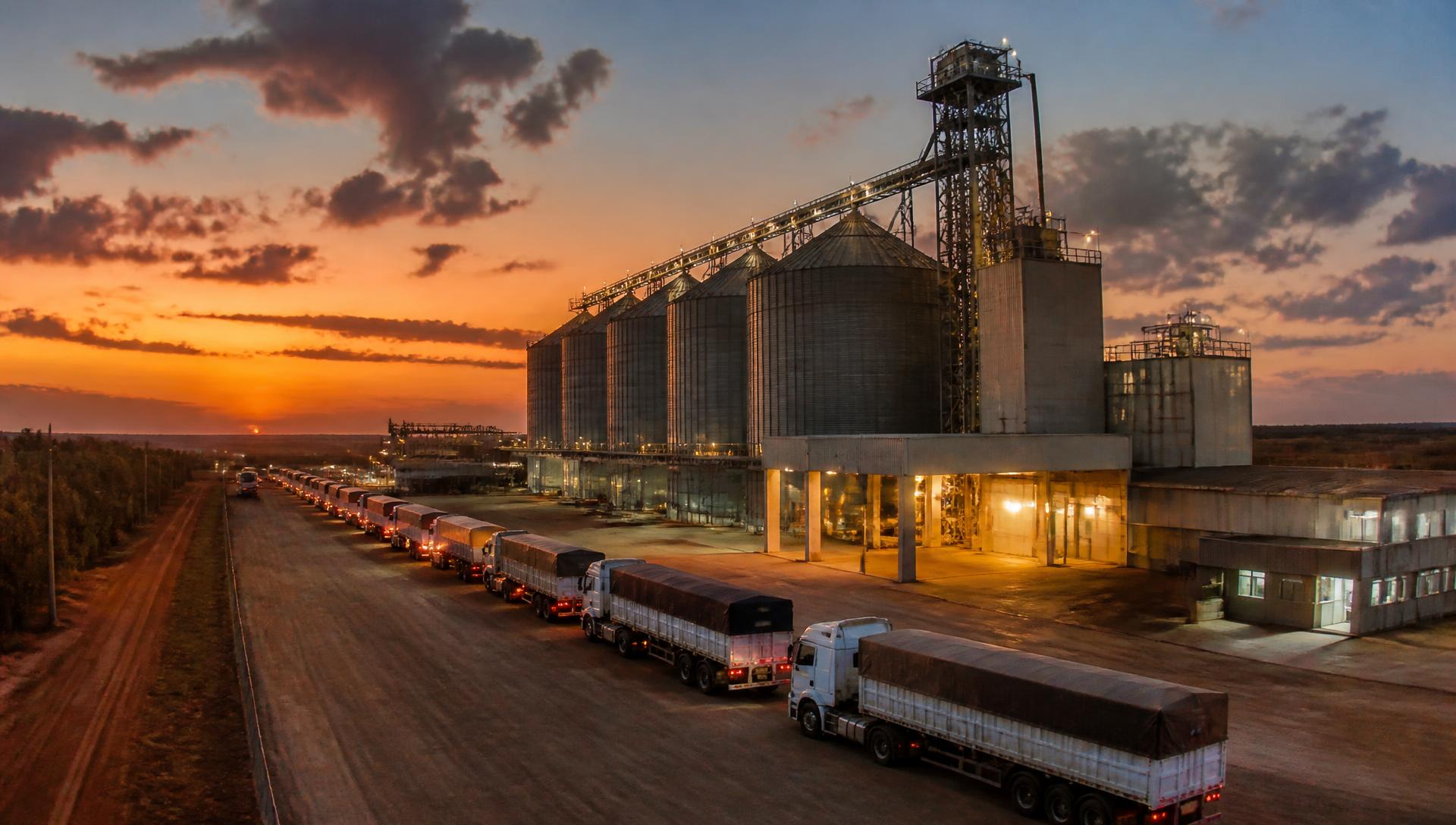 Unidade armazenadora com caminhões graneleiros ao entardecer
